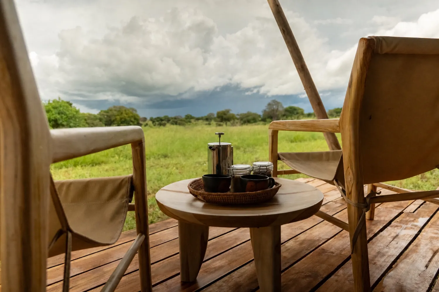 Terraza de un campamento abierta a la sabana, con el caf&eacute; servido sobre una mesa de madera